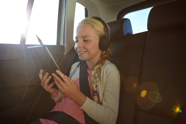 Viagens são mais divertidas com o seu tablet. uma menina viajando em um carro - Foto, Imagem
