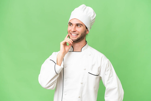 Молодой красивый шеф-повар на изолированном фоне думает об идее, глядя вверх - Фото, изображение