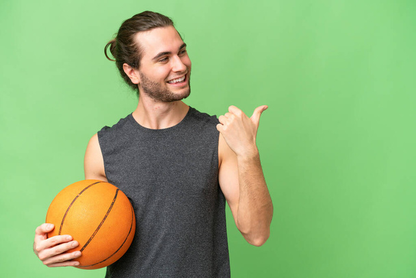 Junger Basketballspieler über isolierten Hintergrund, der zur Seite zeigt, um ein Produkt zu präsentieren - Foto, Bild