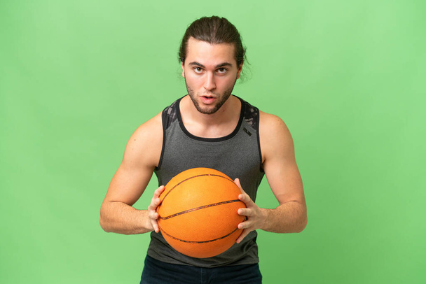 Genç yakışıklı adam yeşil krom arka planda izole edilmiş basketbol oynuyor. - Fotoğraf, Görsel
