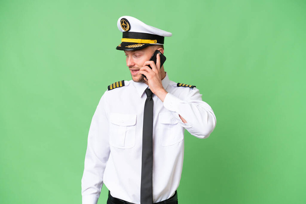 Αεροπλάνο πιλότος άνθρωπος πάνω από απομονωμένο υπόβαθρο κρατώντας μια συνομιλία με το κινητό τηλέφωνο με κάποιον - Φωτογραφία, εικόνα