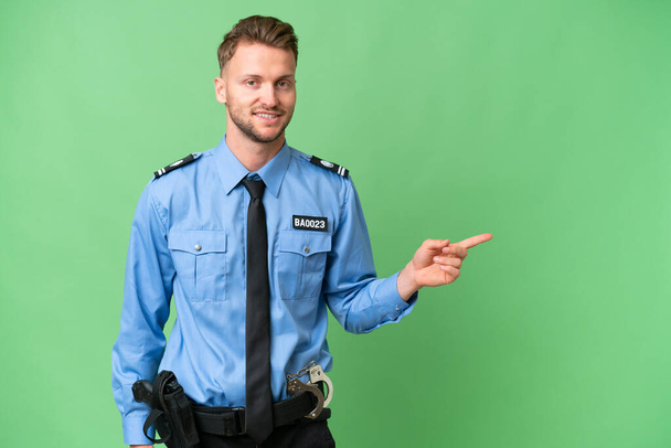 Jonge politieman over geïsoleerde achtergrond wijzend vinger naar de zijkant - Foto, afbeelding