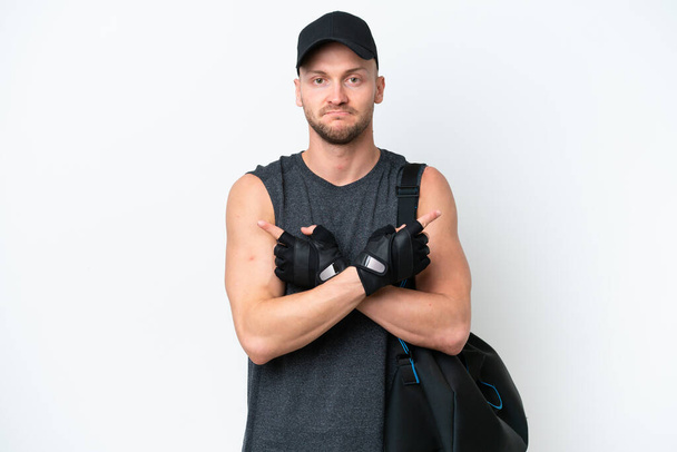 Young blonde sport caucasian man with sport bag over isolated white background pointing to the laterals having doubts - Photo, Image