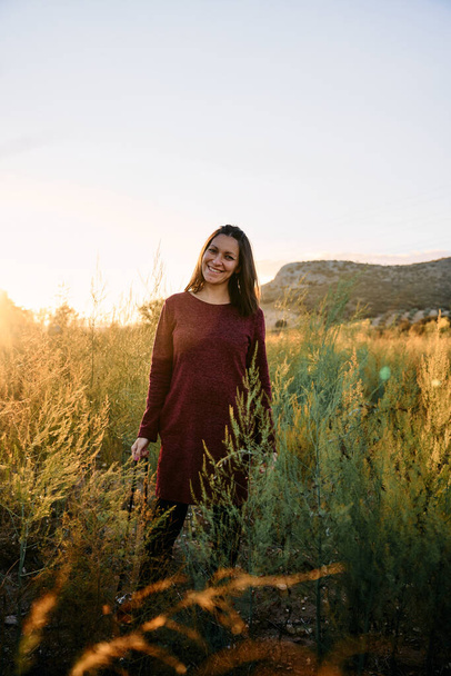 una joven adulta caminando por el prado con su cámara vintage, disfrutando y fotografiando la puesta de sol. - Foto, imagen