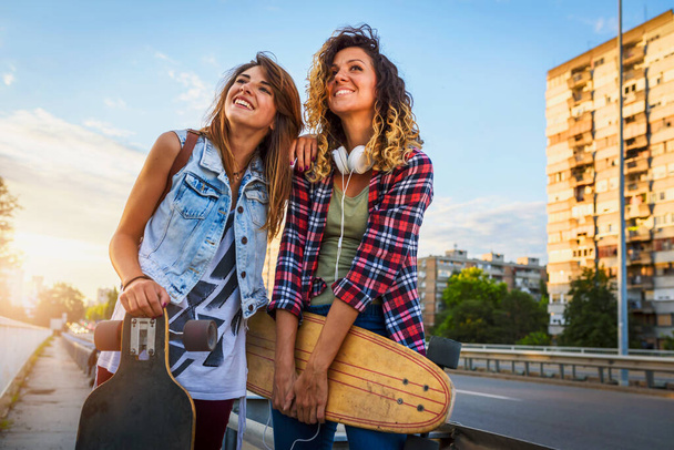 beautiful girls with skateboards walking on the street at sunset - Fotó, kép