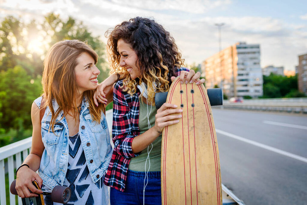 красиві дівчата зі скейтбордами, що ходять на вулиці на заході сонця
 - Фото, зображення