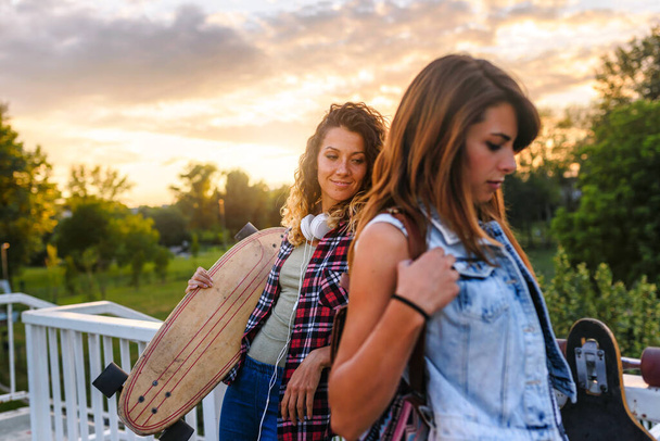schöne Mädchen mit Skateboards, die bei Sonnenuntergang auf der Straße laufen - Foto, Bild