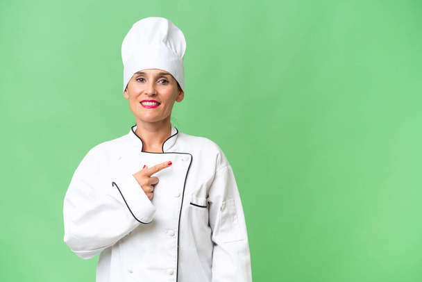 Middle-aged chef woman over isolated background pointing to the side to present a product - Photo, Image