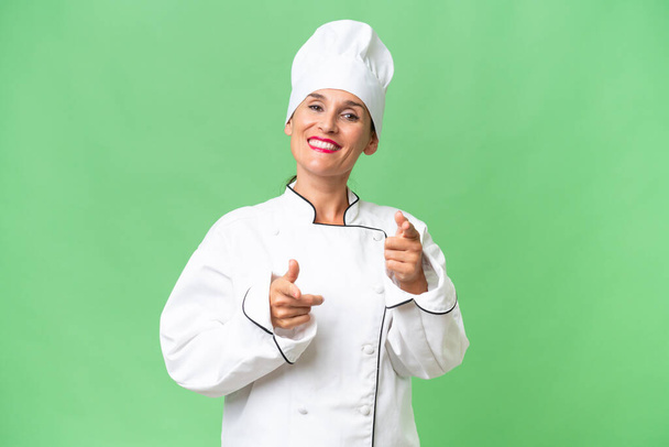 Keski-ikäinen kokki nainen yli eristetty tausta osoittaa eteen ja hymyilee - Valokuva, kuva