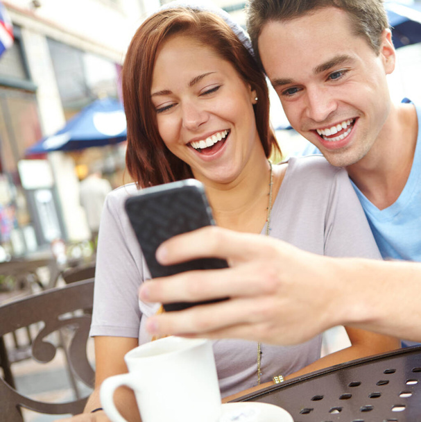 Sharing a funny joke through Social media. A happy couple laughing at something on a cellphone while having coffee at a cafe - Фото, зображення