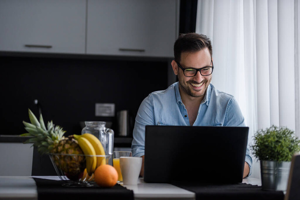 junger Mann mit Laptop arbeitet von zu Hause aus in der Küche - Foto, Bild