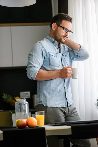 handsome guy is drinking coffee, standing near window  - Zdjęcie, obraz