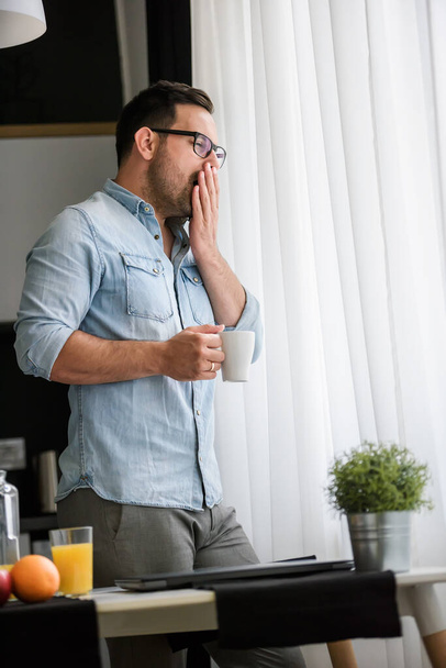 handsome guy is drinking coffee, standing near window  - Photo, Image