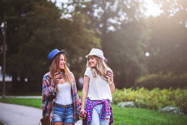 Yeşil parkta yürüyen iki genç kadın. Öğrenci kızlar konuşuyor. En iyi arkadaşlar - Fotoğraf, Görsel