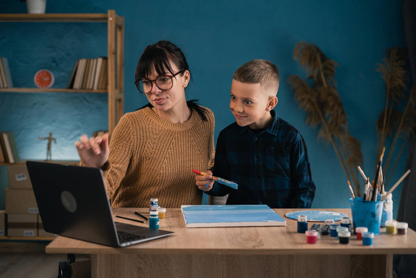 Online education for children. Mother and son schoolboy watching a video lecture on drawing using a computer in the living room. - Фото, зображення