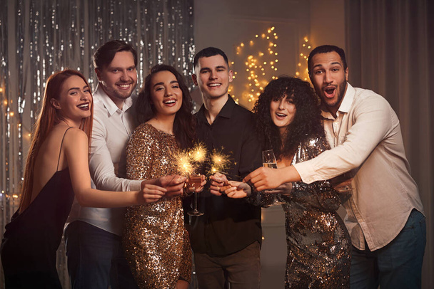 Happy friends with glasses of wine and sparklers celebrating birthday indoors - 写真・画像