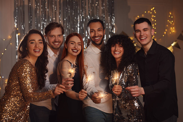 Happy friends with glasses of wine and sparklers celebrating birthday indoors - Zdjęcie, obraz