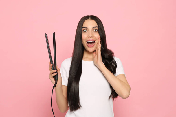 Beautiful emotional woman with hair iron on pink background - Фото, изображение
