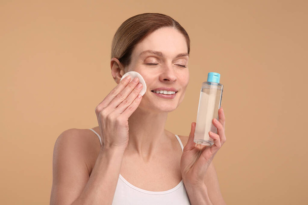 Beautiful woman removing makeup with cotton pad on beige background - Foto, afbeelding