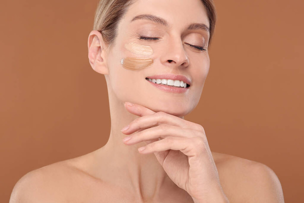 Woman with swatches of foundation on face against brown background - Foto, immagini