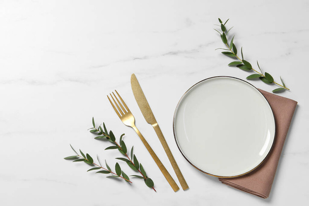 Stylish setting with cutlery and eucalyptus leaves on white marble table, flat lay. Space for text - 写真・画像