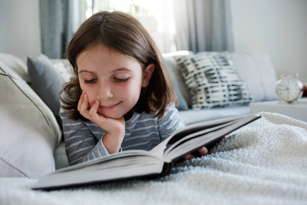 mooi klein meisje lezen boek op de bank  - Foto, afbeelding
