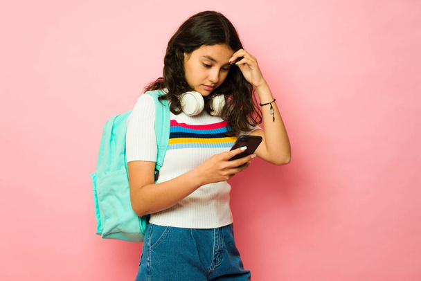 Zamartwiona nastolatka idzie do szkoły i otrzymuje złe wieści podczas pisania na swoim smartfonie patrząc zdenerwowany - Zdjęcie, obraz
