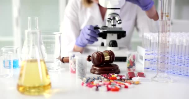Scientist investigates medical pills through microscope in equipped laboratory. Worker checks drugs among judge gavel and bottles with capsules slow motion - Footage, Video