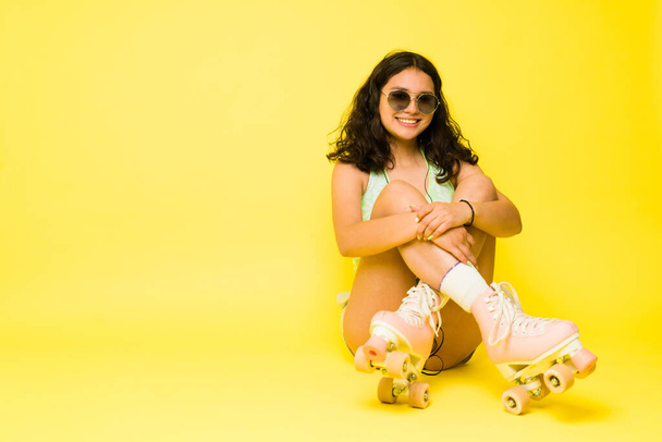 Klasik güneş gözlüklü sevimli genç kız yazın tadını çıkarıyor. Paten giyiyor ve sarı bir stüdyoda dinleniyor. - Fotoğraf, Görsel