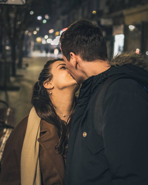 Вертикальний знімок молодої кавказької пари цілується на вулиці вночі
 - Фото, зображення