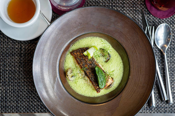 A top-view of a roasted fish served with a green creamy sauce on a plate - Fotó, kép