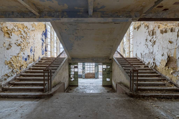 The interior of old abandoned school with symmetric stairways and weathered walls - 写真・画像