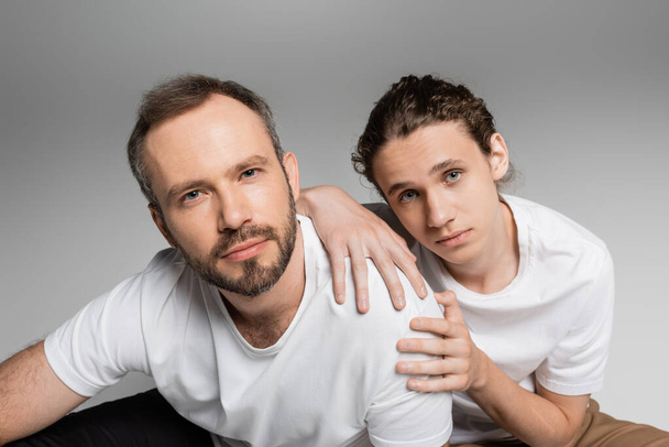 bearded man with his teenage son looking at camera isolated on grey  - Foto, Imagen