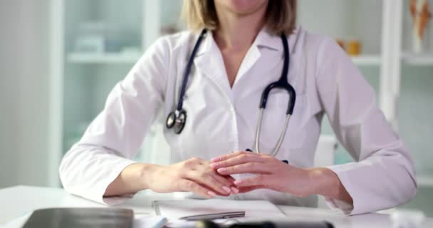 Vrouwelijke arts toont hart met handpalmen zitten aan het bureau in slow motion. Cardioloog toont steun aan patiënten met hartproblemen - Video