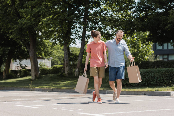 bearded dad and happy teenage son walking with shopping bags outdoors  - Photo, Image