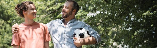 vrolijk man houden voetbal terwijl knuffelen gelukkig tiener zoon buiten, banner  - Foto, afbeelding