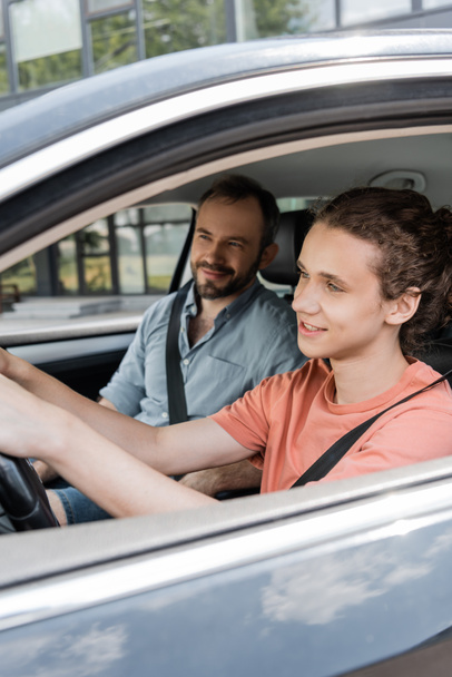 happy teenage boy holding steering wheel while driving car next to dad  - Photo, Image