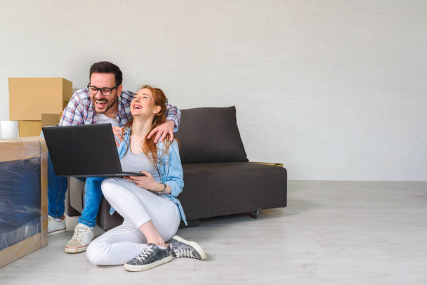 Gyönyörű fiatal pár ül kartondobozok között az új lakásban terveket készítenek laptoppal - Fotó, kép