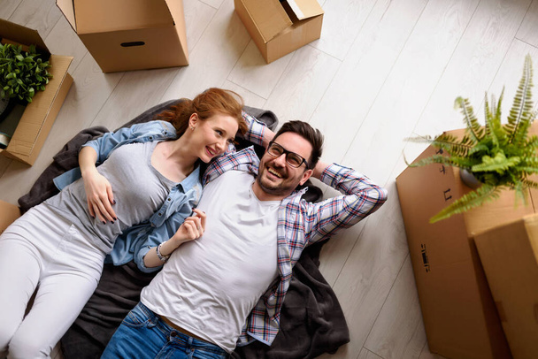 Beau jeune couple couché sur le sol parmi des boîtes en carton dans leur nouvel appartement qu'ils viennent d'emménager. Rêver, faire des projets pour l'avenir. - Photo, image