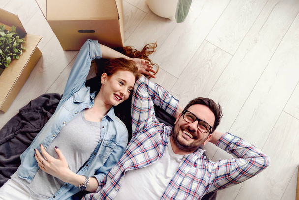 Beautiful young couple lying on the floor among cardboard boxes in their new apartment they just moved in. Daydreaming, making plans for the future. - Foto, Imagem