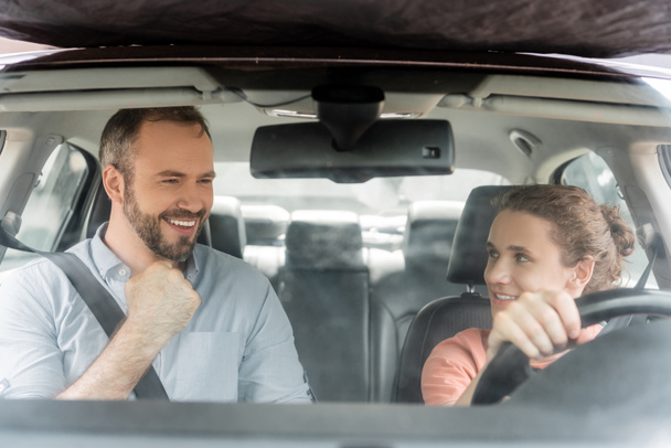 happy teenager boy holding steering wheel and looking at excited father while driving car  - Foto, imagen