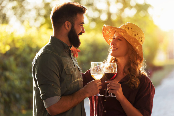 ブドウ畑でワインを飲む若いカップルは  - 写真・画像