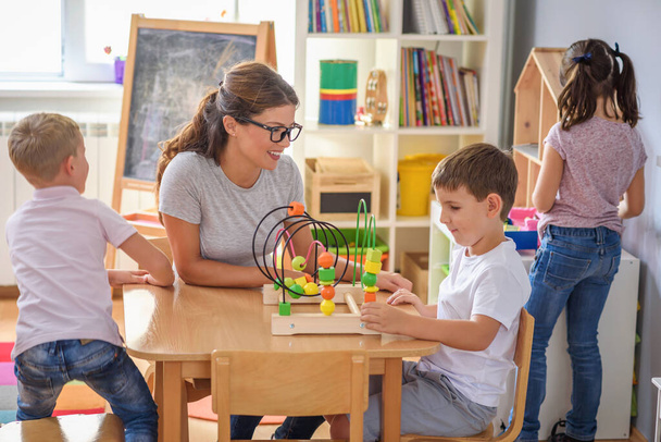 Вчитель дошкільного віку з дітьми грає з барвистими дерев'яними дидактичними іграшками в дитячому саду
 - Фото, зображення