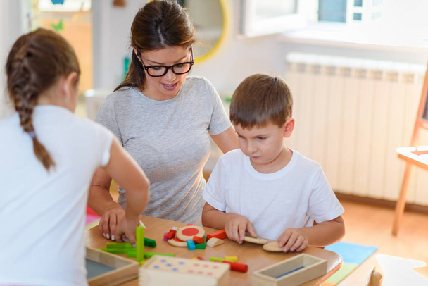 Учитель дошкольного возраста с детьми, играющими с красочными деревянными дидактическими игрушками в детском саду - Фото, изображение