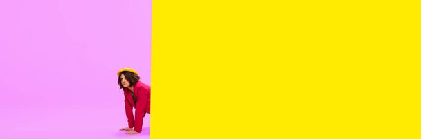 News, journalism. Young girl in stylish clothes peeking out vivid yellow and pink background. Pop art style. Concept of art, creative vision, fashion. Complementary colors. Banner. Copy space for ad - Photo, Image