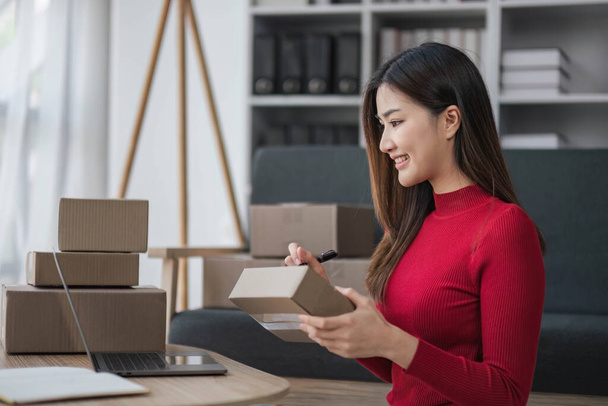 Startup small business entrepreneur SME, asian woman packing cloth in box. Portrait young Asian small business owner home office, online sell marketing delivery, SME e-commerce telemarketing concept - Φωτογραφία, εικόνα