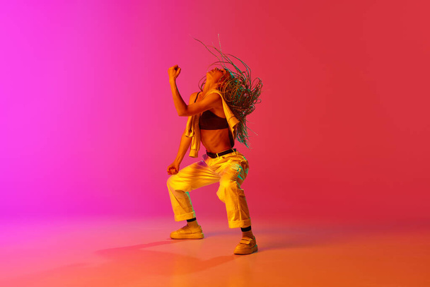 Contemporary choreography. One professional hip-hop dancer wearing fashion clothes moving with inspiration over gradient pink background in neon light. Concept of modern dance, motion, hobby, art, ad - Foto, Bild