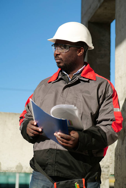 Obrero afroamericano se para en obra con papeles de trabajo - Foto, Imagen