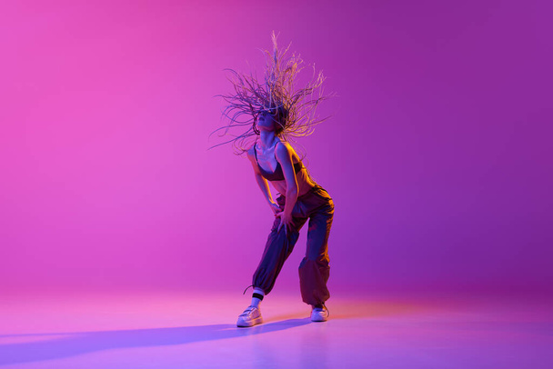 Portrait with young adorable girl, dancer with flying hair dancing over gradient purple background in neon light. Concept of contemporary dance style, motion, art, movement, inspiration, hobby, ad - Photo, Image