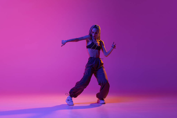 Liberty of dance. Portrait with modern young dancer wearing fashion clothes in motion over puple background in neon light. Contemporary dance style, motion, art, movement, youth culture, ad concept - 写真・画像